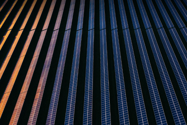 Aerial view of blue solar panels arranged in parallel rows across dark ground as part of a solar farm (from above).