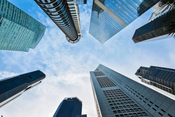 Look-up view of tall modern skyscrapers encircling a blue sky, forming a canyon of glass and steel.