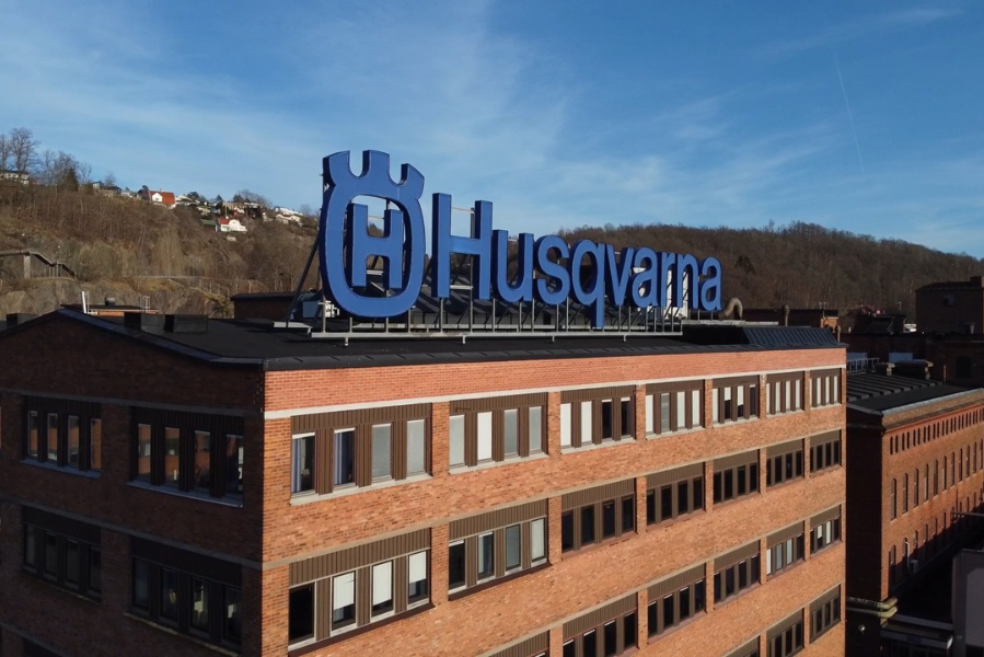 Blue Husqvarna sign on top of a brick office building, hillside in the background under a clear blue sky
