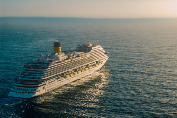 A large white cruise ship gliding through calm blue ocean at sunset.