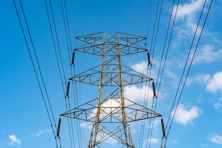 High-voltage transmission tower with multiple power lines against a blue sky.